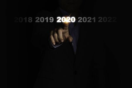 Businessman hand touching 2020 year on black background. It is symbol of fiscal and business year change.の写真素材