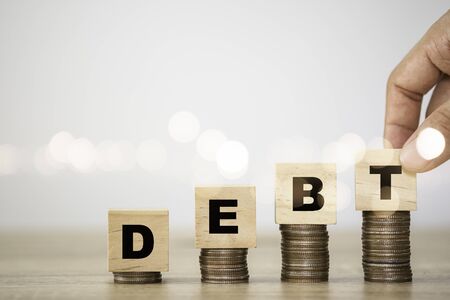 Hand putting debt wording which are printed screen to wooden cubes on coins stacking. Debt...