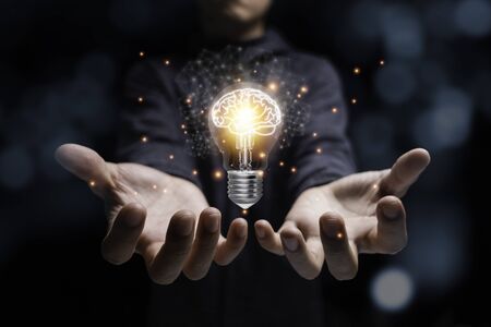 Businessman holding glowing lightbulb with virtual brain and orange light . Creative new business...