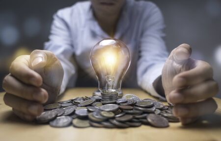 Businessman hand protecting heap of coins and light bulb which glowing. Creative new business idea can make profit money concept.の写真素材
