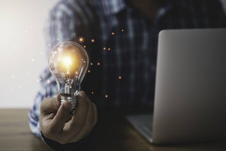 Businessman hand holding lightbulb with orange glowing and creative idea to laptop.の写真素材