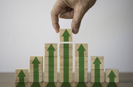 Hand putting wooden cubes block which print screen increase or up green arrow. It is symbol of...