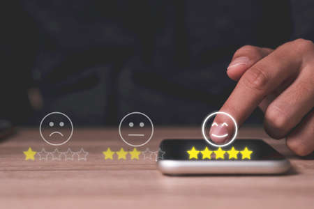 Hand touch on mobile phone to add five yellow stars to customer evaluates products and services. Customer satisfaction and marketing survey rating concept.の写真素材