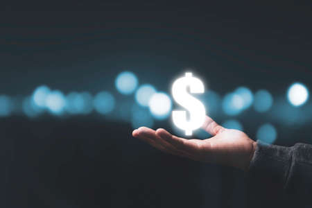 Businessman holding virtual US dollar sign with beautiful bokeh background. USD is main exchange...