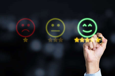 Customer satisfaction service and product concept , Businessman drawing gold star with smile face to submit evaluation scorecard.の写真素材