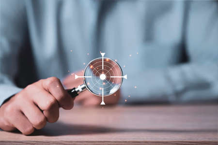 Focus in objective target and goal concept, businessman manager holding magnifier glass with virtual target board on wooden table with copy space.の写真素材