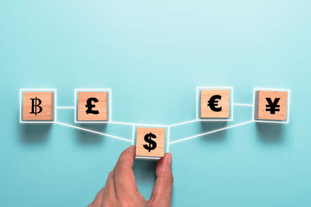 Hand holding US dollar sign print screen to wooden cube and link with yuan yen euro and pound sterling. Currency exchange and forex concept.の写真素材