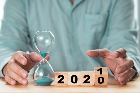Businessman flipping 2020 to 2021 wooden cubes box with hourglass on wooden table.