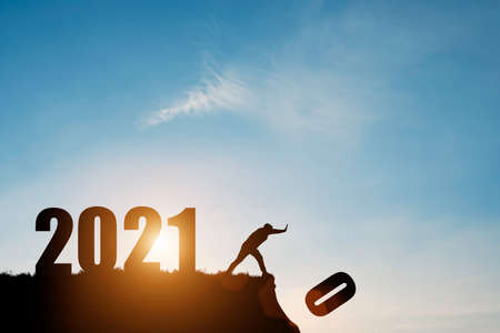 Man push number zero down the cliff where has the number 2021 with blue sky and sunrise. It is...