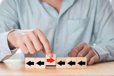 Disruption  and different thinking concept , businessman holding red arrow among black arrow which print screen on wooden cube block and it opposite direction.の写真素材