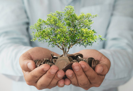 Businessman holding coins in hand with growth tree, investment profit and dividend money from saving concept.の写真素材
