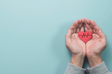Businessman hand holding red heart paper with heart wave signal on blue background. It is health...