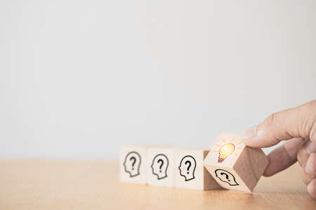 Hand flipping wooden cube block which print screen face with questions mark to lightbulb, creative...