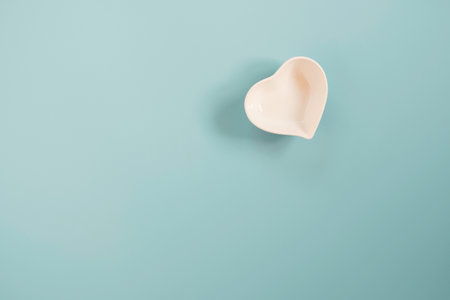White small ceramic heart shape bowl on blue and copy space on blue background for...