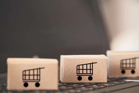 Trolley or shopping cart logo on small cartons boxes lay on keyboard computer laptop for online shopping and service delivery to customer concept.の写真素材