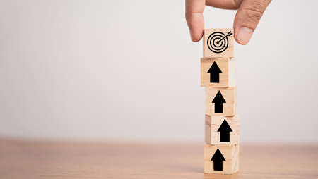 Hand putting target board on up arrows which print screen on wooden cube block, increasing and challenge of setup business achievement objective target concept.の写真素材