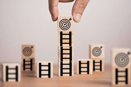 Hand putting target board on the top of ladder which print screen on wooden cube block, setup challenge achievement objective in business and life concept.の写真素材
