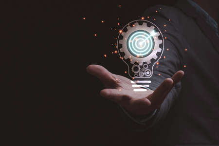 Businessman holding virtual lightbulb which contain mechanical gear and target board, creative thinking idea for business achievement concept.の写真素材