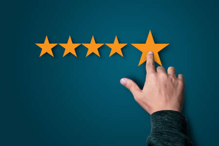 Businessman touching to five yellow stars on dark blue background, the best customer satisfaction and evaluation for good quality product and service.の写真素材