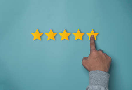 Hand touching to golden yellow stars on blue background for customer satisfaction of quality product...