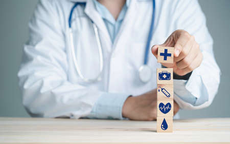 Doctor hand holding wooden stacking with healthcare medical and hospital icons on table , Health and insurance concept.の写真素材