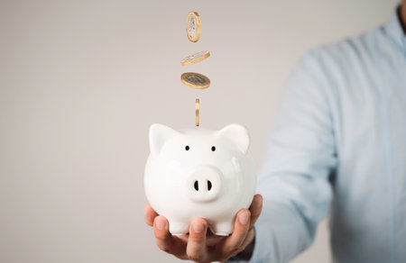 Businessman holding white piggy with coins falling for money saving and deposit concept.の写真素材