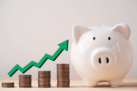 White piggy bank saving and coins stacking with increasing green arrow for money saving and deposit concept.の写真素材