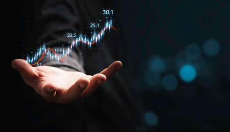 Trader hand holding smartphone with stock market graph chart on dark background for technical...