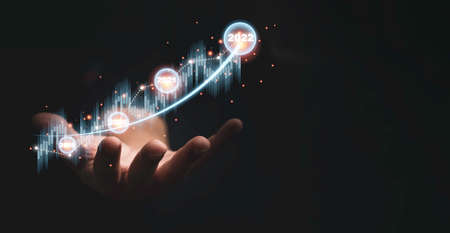 Trader hand holding virtual stock market graph chart on dark background for technical investment analysis concept.の写真素材