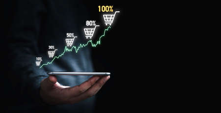 Businessman holding smartphone which display virtual graph chart and shopping trolley cart for ...