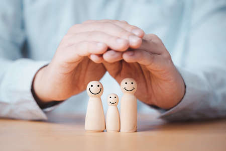 Business hand gesture protecting wooden family dolls for insurance and assurance concept.