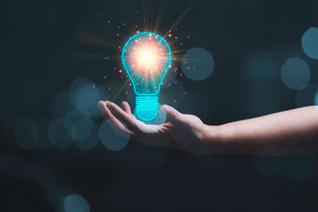 Businessman holding glowing drawing light bulb with orange light ray on wooden table for inspiration...