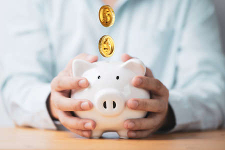 Businessman holding white piggy bank saving with golden coins falling for deposit and money saving...