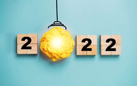 Light bulb from yellow scrap paper with 2022 year on wooden cube block for happy new year idea and...