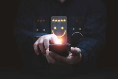 Businessman using smartphone for select smiley face icon for client evaluation and customer satisfaction after use product and service concept.の写真素材
