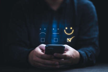 Businessman using smartphone for select smiley face icon for client evaluation and customer satisfaction after use product and service concept.の写真素材