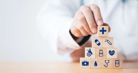 Doctor putting and stacking wooden block cube which print screen health care and medical icons for healthy and wellness concept.の写真素材