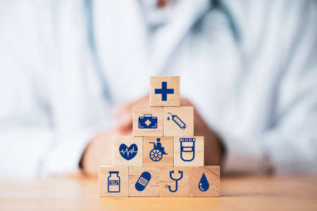 Doctor putting and stacking wooden block cube which print screen health care and medical icons for healthy and wellness concept.の写真素材