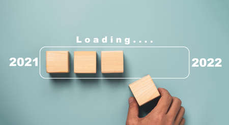 Hand putting wooden cube block for downloading progress for countdown 2021 to 2022 on blue background for Merry Christmas and happy new year preparation concept.の写真素材