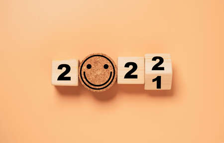 Wooden cube block flipping from 2021 to 2022 with smile face on orange background , preparation for merry Christmas and happy new year and 3d rendering concept.の写真素材