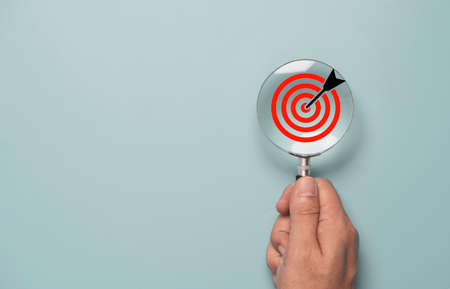 Hand holding magnify glass with red target board inside for focus and setup business objective...