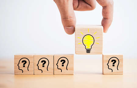 Hand holding lightbulb drawing which print screen on wooden cube block among human and question mark...