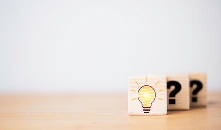 Drawing glowing lightbulb in front of question mark which print on wooden cube block for question answer and problem solving solution concept.の写真素材