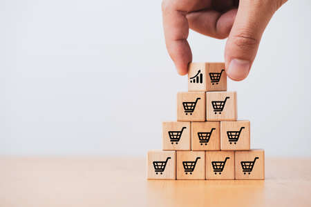 Hand holding wooden cube block stacking which print screen shopping trolley cart and investment graph for sale amount increasing and business growth concept.の写真素材