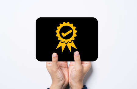 Hand holding black card with golden quality assurance and guarantee certificate sign.の写真素材