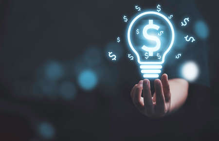 Businessman holding virtual lightbulb or lamp with dollar sign for creative idea can make more money concept.の写真素材