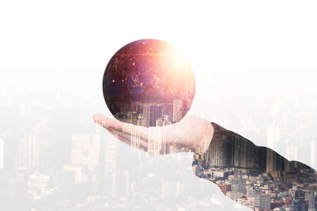 Double exposure of hand holding globe with growing light with city scape for global business concept