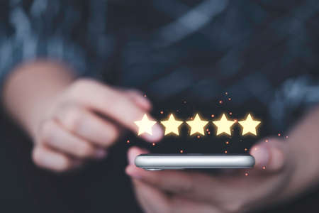 Businesswoman using smartphone  with yellow glowing five stars for client customer review product...