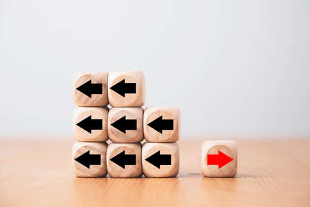 Red arrow on wooden move on different direction with black arrow on cube for business and technology disruption or unique concept.の写真素材