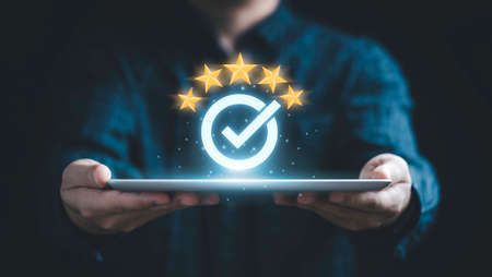 Businessman holding tablet and showing the best quality assurance with golden five stars for guarantee product and ISO service concept.の写真素材